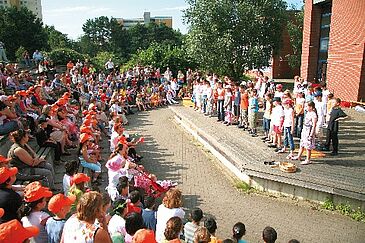 Kinder sitzen im Halbkreis im Freien